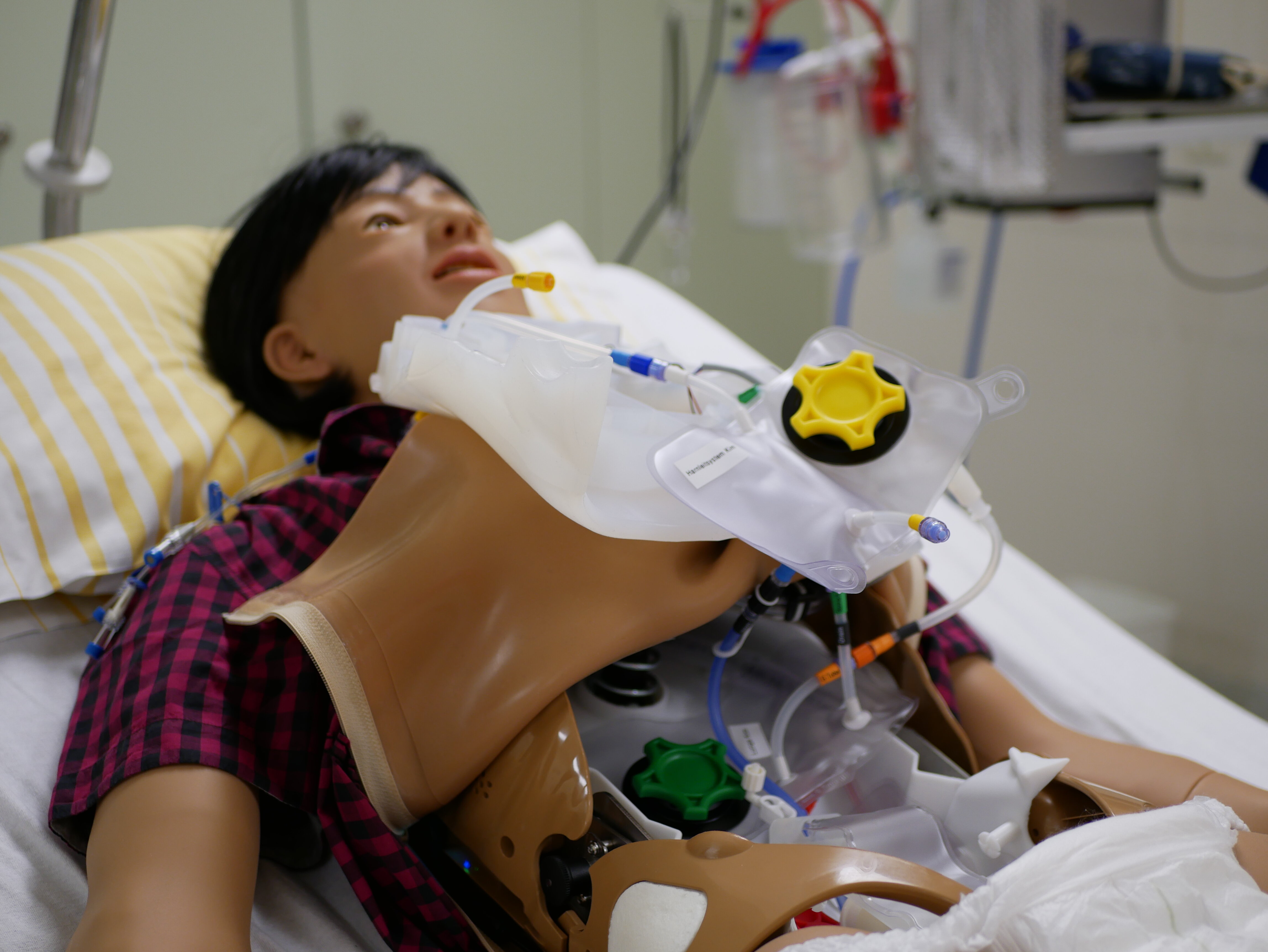 Simulator liegt im Bett. Die technischen Details und befüllbaren Beutel im Bauchraum schauen heraus. 